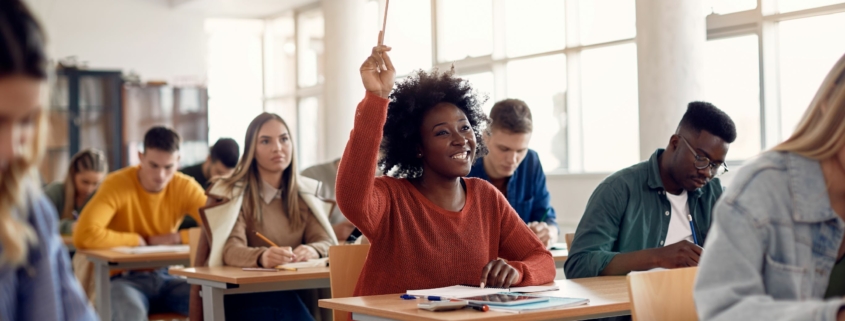 university student raising her hand with a pencil to ask or answer a question in a classroom setting